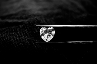 Front view of a heart-shaped moissanite gemstone held by tweezers, showcasing brilliant facets and perfect symmetry.