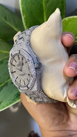 Side view of a men’s VVS moissanite watch, fully iced out with shimmering stones, held in hand against green leaves.
