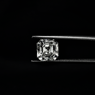 Front view of an Asscher cut Moissanite loose stone held by tweezers against a black background.