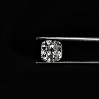 Front view of a cushion-cut moissanite held by metal tweezers against a black background, showcasing its brilliance and faceting.