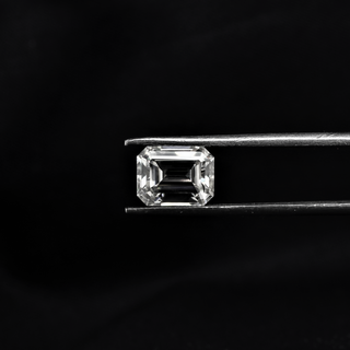 Front view of an emerald cut moissanite held by tweezers, highlighting its step-cut facets and mirror-like clarity.