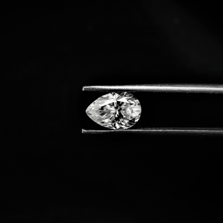 Front view of a pear-cut moissanite gemstone held by tweezers on a black background, displaying its sparkle and elegant shape.