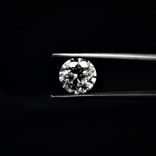 Front view of a round brilliant-cut moissanite held by tweezers against black background, highlighting sparkle and symmetry.